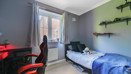Single bedroom set up with bed, desk, shelving and window overlooking neighbouring buildings