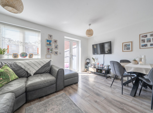 Living room with a corner sofa, dining table, TV and patio doors.