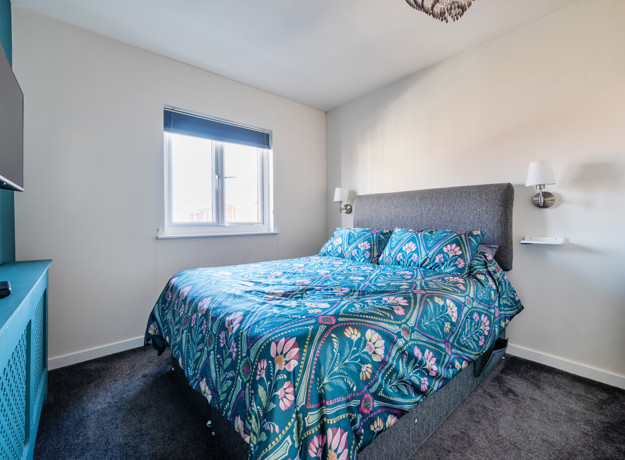 Bedroom with patterned bedspread, wall-mounted TV and window.