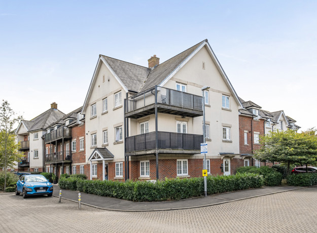 Exterior view of apartment building with balconies and parking area.