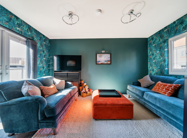 Living room with sofas, television, window, patio doors and red footstool.