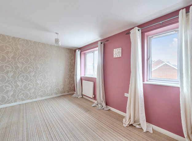 Living room with patterned wallpaper, pink walls, and windows with light curtains.