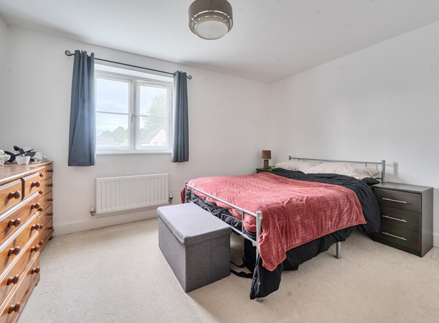 Bedroom with bed, chest of drawers, wardrobe and window with curtains.