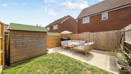 Small garden with lawn, shed, patio seating, and fenced boundaries.