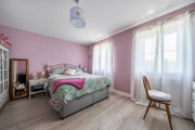 Bedroom with double bed, chair, and windows with curtains.