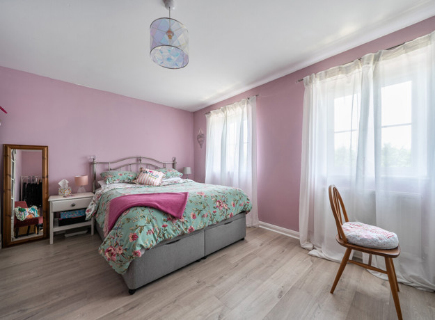 Bedroom with double bed, chair, and windows with curtains.