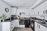 White kitchen with black countertops, appliances, sink, and overhead cabinets.
