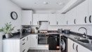 White kitchen with black countertops, appliances, sink, and overhead cabinets.