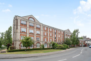 Red brick apartment building on a street corner with trees and road.