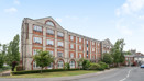 Red brick apartment building on a street corner with trees and road.