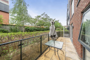 Balcony with glass railing, table, chair, and garden view.