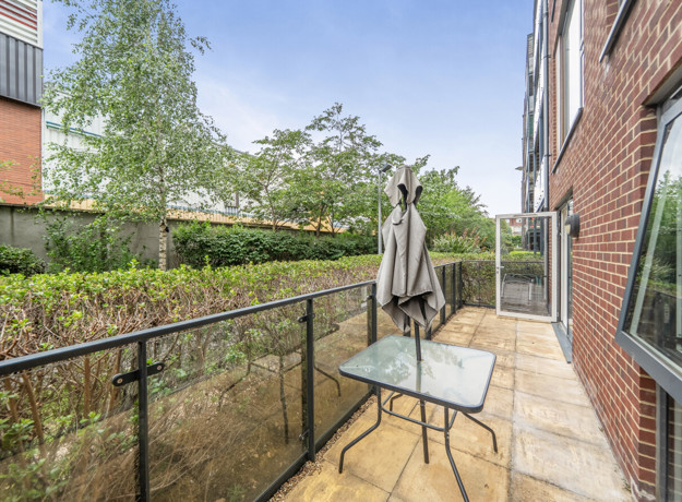 Balcony with glass railing, table, chair, and garden view.