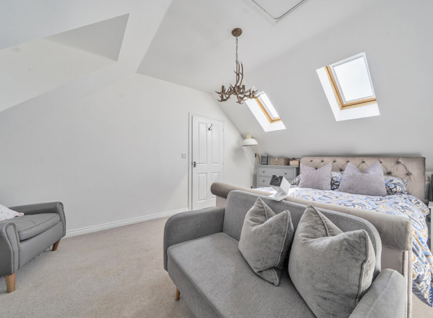Loft bedroom with double bed, skylights, seating area and hanging ceiling light.