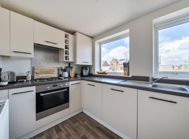 Kitchen with white cabinets, oven, hob, and window overlooking nearby buildings.