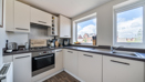 Kitchen with white cabinets, oven, hob, and window overlooking nearby buildings.