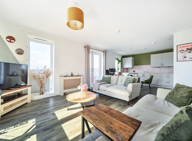 Living area with sofas, coffee table, television, and windows and kitchen in the background.