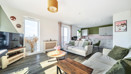 Living area with sofas, coffee table, television, and windows and kitchen in the background.
