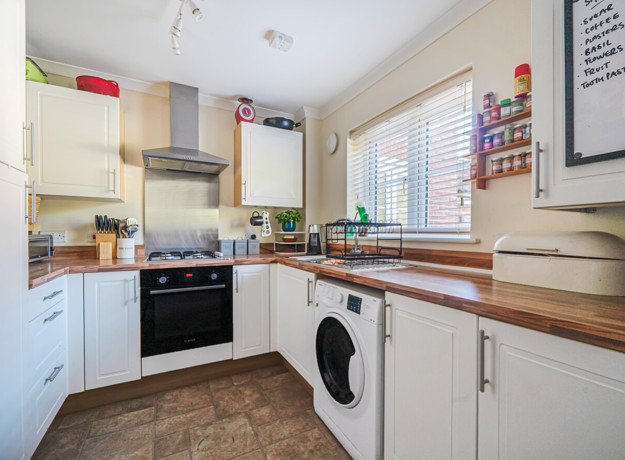 Fitted kitchen with white cabinets, wooden worktops, appliances and tiled flooring
