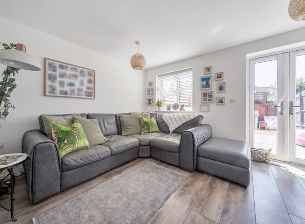 A white painted living room with grey corner sofa, pictures on the wall and patio doors to the right