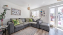 A white painted living room with grey corner sofa, pictures on the wall and patio doors to the right