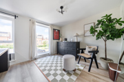 Second bedroom with desk, chair, patterned floor, plants, and large window.