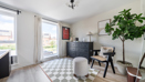 Second bedroom with desk, chair, patterned floor, plants, and large window.