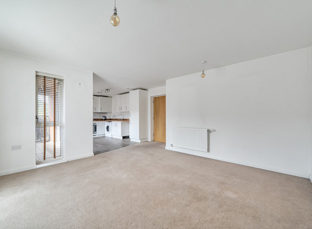 Open-plan living area with carpeted floor and kitchen in the background.