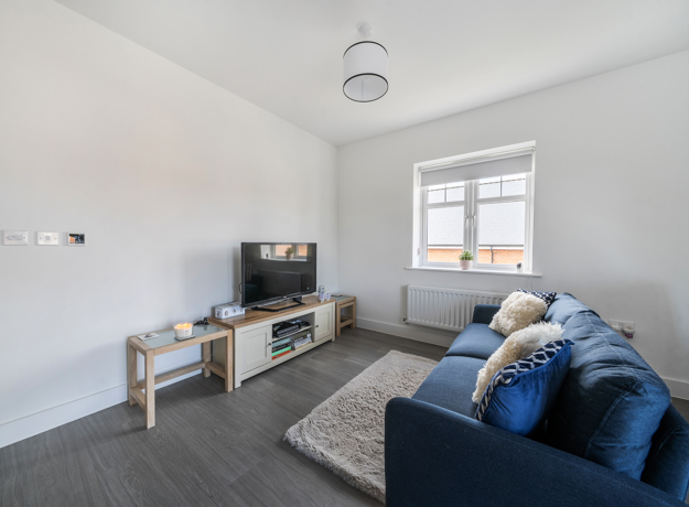Living room with blue sofa, TV stand, rug, window, and grey flooring throughout.