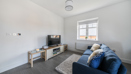 Living room with blue sofa, TV stand, rug, window, and grey flooring throughout.