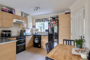 Kitchen with wooden-effect cabinets, appliances and small dining table with chairs.
