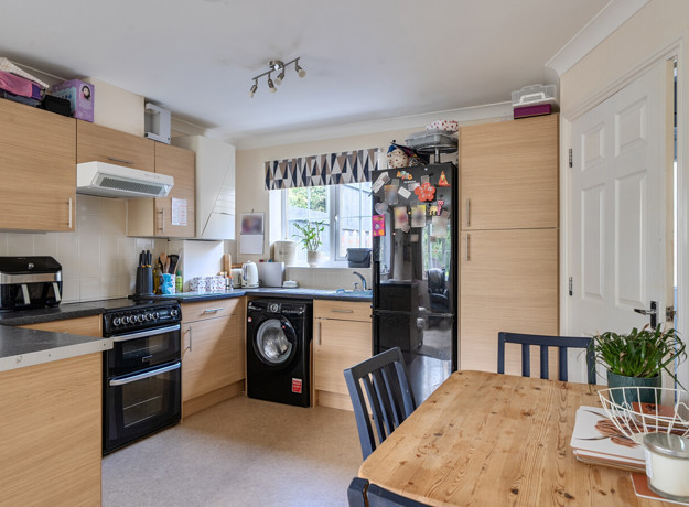 Kitchen with wooden-effect cabinets, appliances and small dining table with chairs.