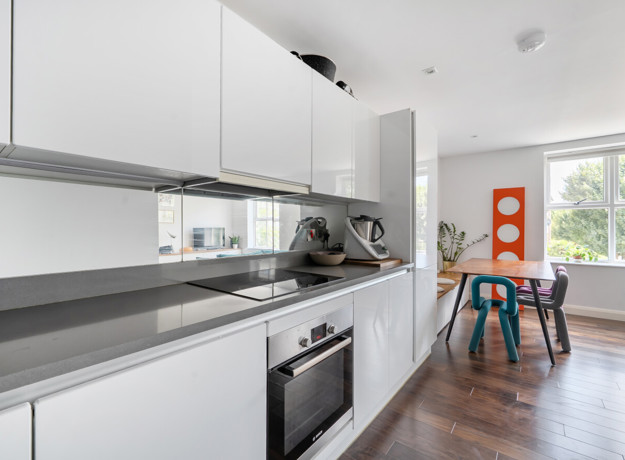 White galley kitchen with integrated appliances and dining area beyond.