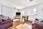 Bright living room with wooden-effect flooring, sofas, large window and TV unit