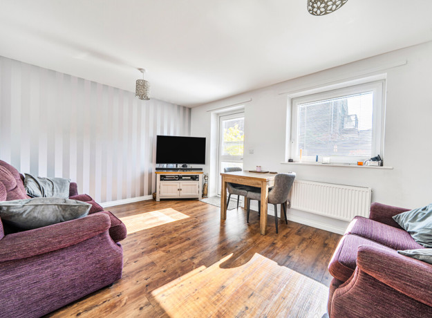 Bright living room with wooden-effect flooring, sofas, large window and TV unit