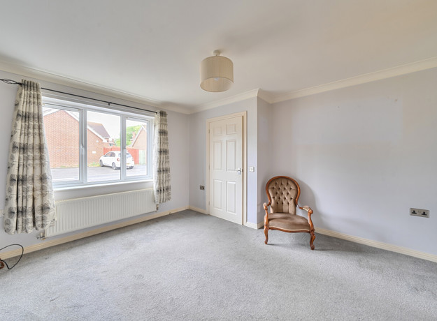 Empty living room with large window, beige carpet, and a single chair by the wall.