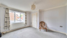 Empty living room with large window, beige carpet, and a single chair by the wall.