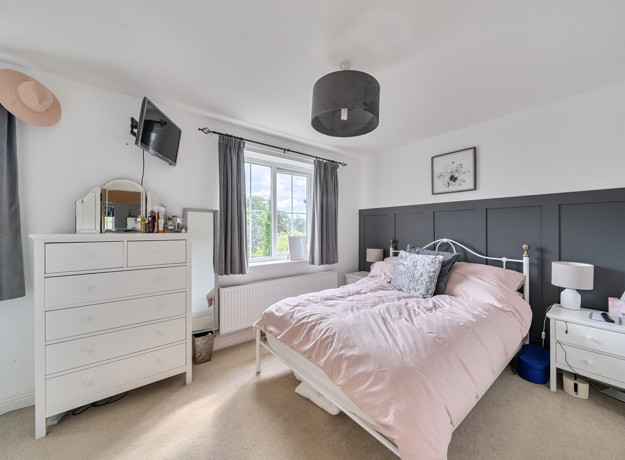 Bedroom with double bed, dresser, bedside tables with lamps and grey curtains by window.