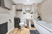 Bathroom with a bath, toilet, sink, mirror and tiled walls.