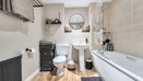 Bathroom with a bath, toilet, sink, mirror and tiled walls.