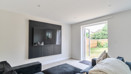 Living room with dark sofa, wall-mounted TV, and glass door opening to a garden.
