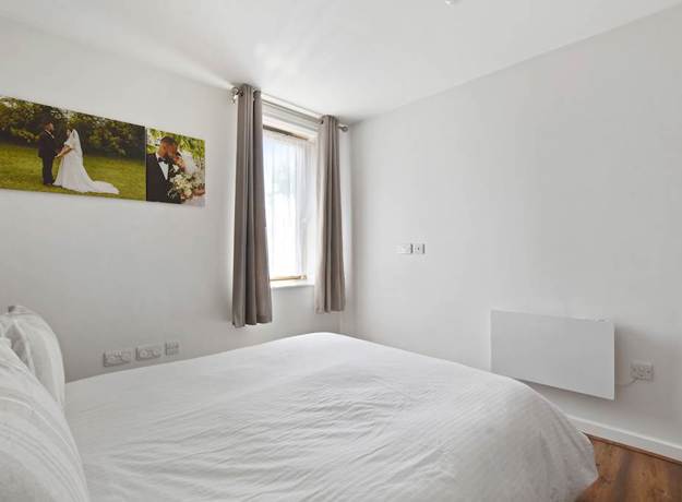 Bedroom with bed, wall art, window, curtains, and wooden flooring.
